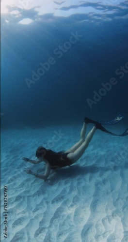 Freediver woman with diving fins glides underwater in tropical blue ocean