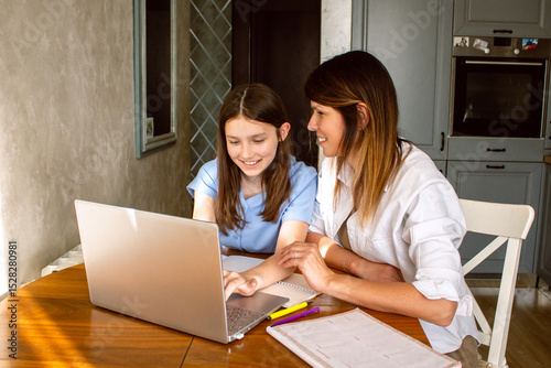 Family digital leisure time. Caucasian mother and daughter using laptop doing online activities, surfing internet, making video call in home interior.