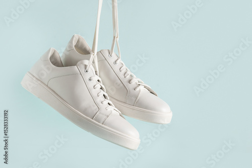 New white sneakers hanging against light blue background. Creative shoes modern style, fashion concept. Summer womens footwear. Copy space.