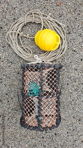 One fishing lobster crab creel pot trap with rope and yellow buoy on the rocky ground.Summer hobby.