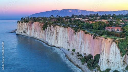Coastal cliffs meet the sea, lush greenery clinging to the dramatic white and pink formations, overlooking a residential area