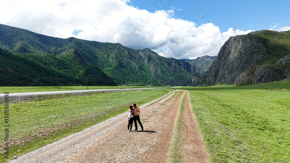 Fototapeta premium A couple travels through the Altai Republic. A couple kisses while walking along the road against the backdrop of mountains. Mountain trips for two. Traveling around Russia.