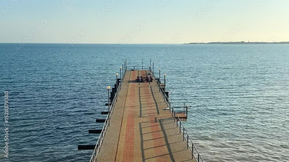 Symmetrical view of long pier stretching into sea under clear sky, perfect for themes of travel, solitude, symmetry, and calm seascapes Symmetrical view of long pier stretching into sea under clear sky, perfect for themes of travel, solitude, symmetry, and calm seascapes