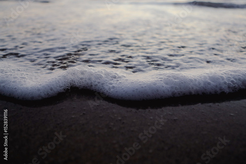 Fototapeta Naklejka Na Ścianę i Meble -  Gentle wave and bubbles on the beach after sunset