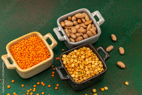 Various legumes displayed in bowls on a green surface during indoor daylight