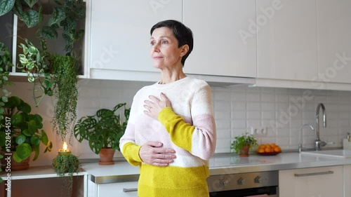 Content serene older woman practicing deep breaths in meditation, hands on torso at home. Stress relief through controlled breathing, comfortable leisure activity, holistic wellness, mindful happiness
