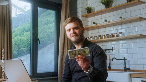 Bearded man in black shirt smiles while holding a stack of U.S. hundred-dollar bills, suggesting success, wealth, or financial reward. photo