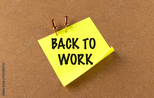 Back to work message on yellow sticky note pinned to corkboard with pushpins as motivational reminder photo