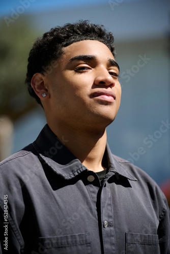 Smiling Dominican man wears a dark shirt and diamond earrings, showing a confident expression. His full lips and natural charm highlight a friendly and stylish personality in this close-up portrait.