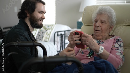 In a cozy living room, a grandson eagerly shows photos to his grandmother on his smartphone, sparking joy and shared memories between them.