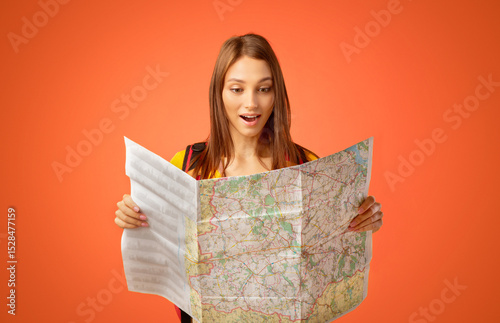 Excited young woman tourist holding city map, yellow studio background. Amazed lady holding map, looking for new destinations to travel, impressed by great travelling opportunities, copy space