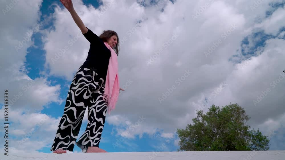Mujer corriente haciendo equilibrio para poder llegar a fin de mes, un día soleado con cielo azul y nubes.