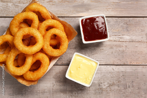 Wall Mural Paper box with fried breaded onion rings and different sauces on grey wooden bac