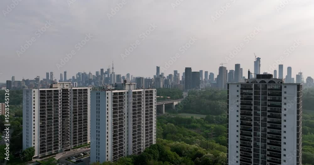 Static wide aerial drone footage of the Toronto skyline, including an iconic Tower, with apartment buildings and the Don Valley in the background and foreground respectively. 