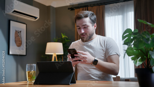 Man working at home, preparing for an online meeting. He sits at a desk with a laptop, engaging with focus and enthusiasm in a modern, cozy home