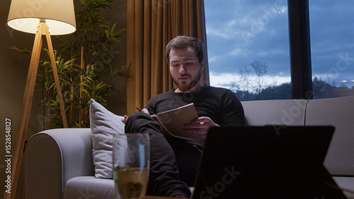 Man reading notebook on sofa in evening