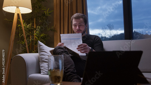 A man sitting on a cozy sofa in living room, attentively reviewing documents. Working on bills, financial planning, or reports.