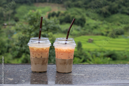 Iced thai tea on wooden table with mountain landscape view. Holiday vacation relax in nature.