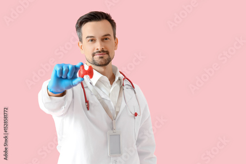 Male endocrinologist with thyroid gland model on pink background