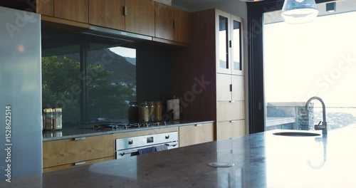 Modern kitchen showcasing marble island, wood cabinets, glass jars, pendant lights, terrace view