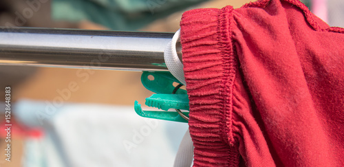 Plastic pegs grip fabric on shiny drying rod. Laundry day with colorful clips on hanging bar. Dry clothes clipped on rack with plastic pegs. Clothespins on drying rack with colorful garments photo