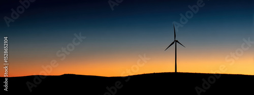 Wind turbine silhouette against vibrant sunset sky evokes sense of tranquility