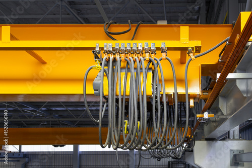 Overhead crane in factory or warehouse. Industrial machine or lifting equipment with hoist, hook and wire rope on beam girder structure for manufacturing production and freight shipping transport.