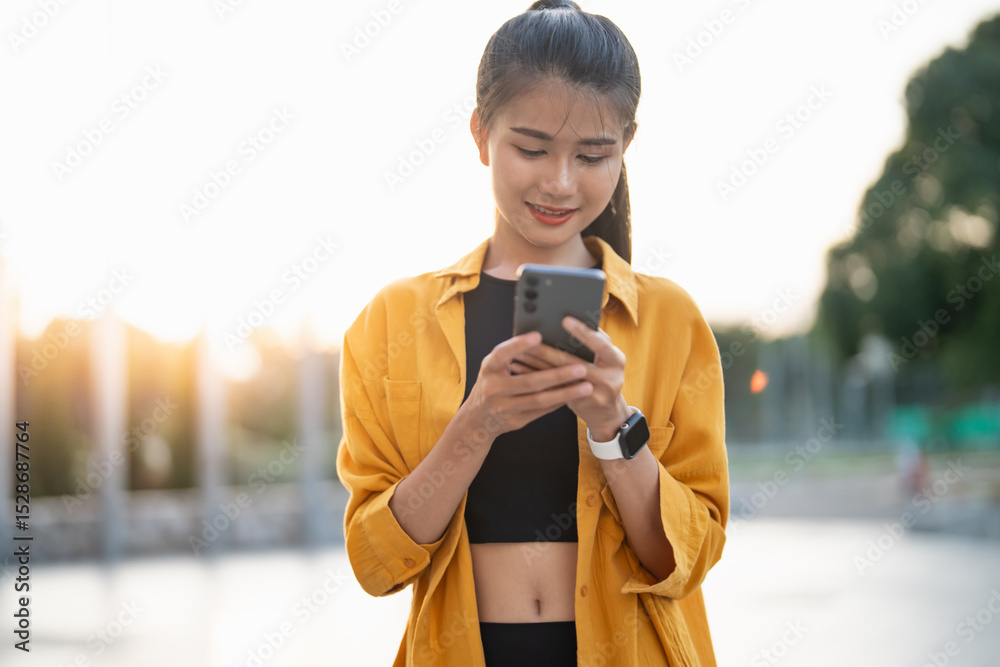 Fototapeta premium Smiling young Asian woman using smartphone in urban city checking apps mobile outdoors