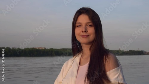 portrait of a beautiful young woman against a stunning river landscape at sunset in the golden hour