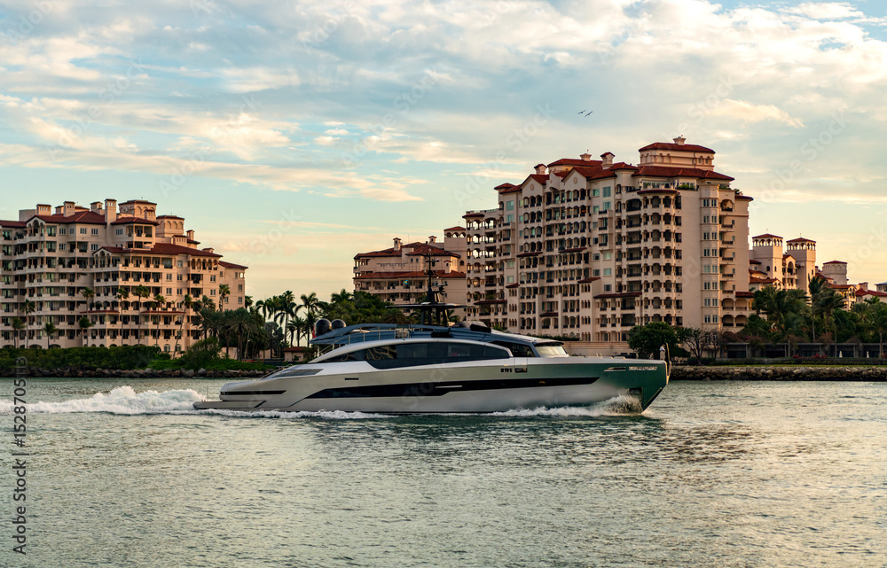 Obraz premium Motor boat yacht floating to marina. Luxury yacht boat at Fisher island. Summer vacation. Fisher island residential building and luxury yacht boat. Trip to Fisher island on yacht, Miami