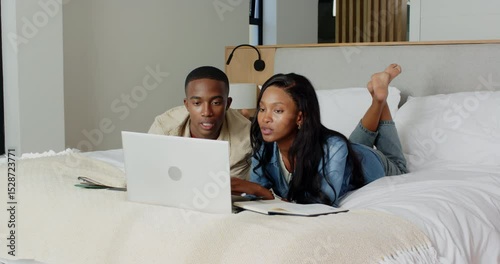 Settling on bed African American couple using laptop, showing tablet and scrolling phone in bedroom