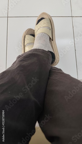 A pair of legs wearing black pants,  socks and brown sandals