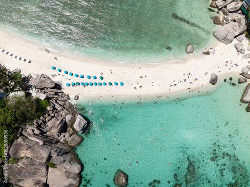 Sandy beach lined with umbrellas surrounded by clear turquoise waters and vibrant scenery. Thailand, Koh Tao.