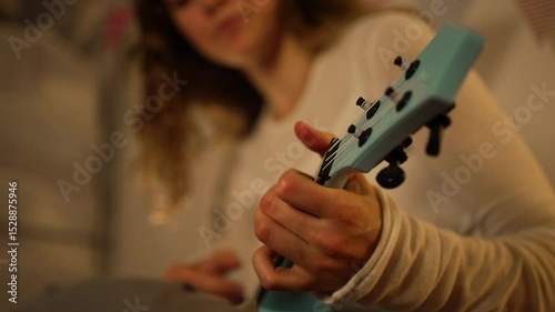 Young woman guitarist performing blue electric guitar, concentrating intently while fingers sliding across strings, capturing passionate musical performance with focused energy