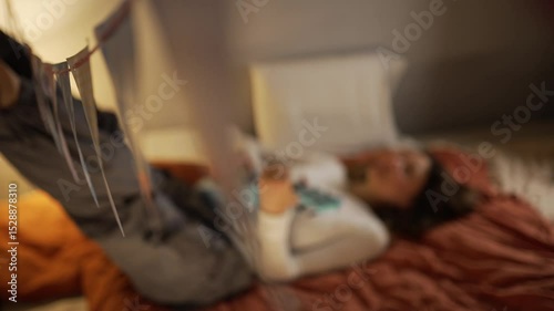 Relaxed young woman lying on bed with legs raised against wall, playing ukulele while enjoying peaceful moment of musical creativity and personal leisure