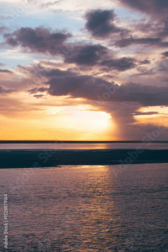 Majestic sunset over serene water with dramatic clouds and reflections in a tranquil coastal landscape