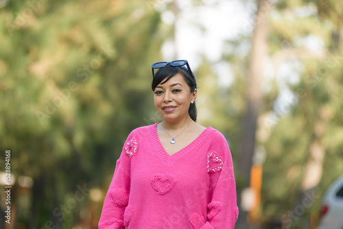 A smiling woman in a vibrant pink sweater adorned with heart details outdoors