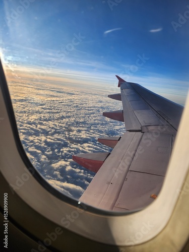 Aerial view from inside a flying airplane, capturing the wing stretching out above the clouds under the open sky.