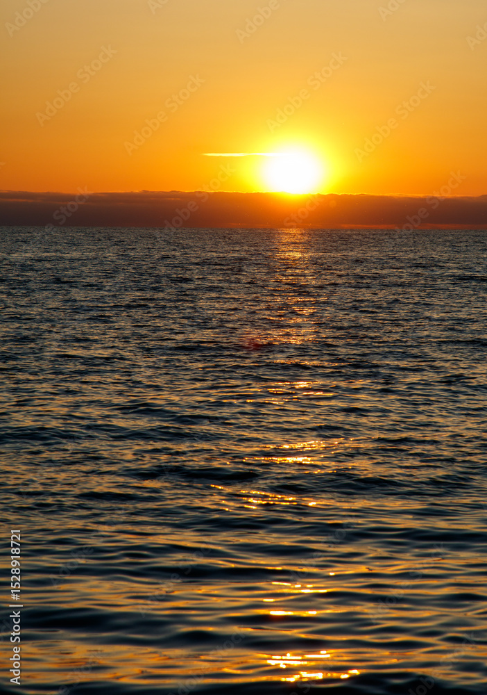 Obraz premium The sun is setting over the ocean, casting a warm glow on the water