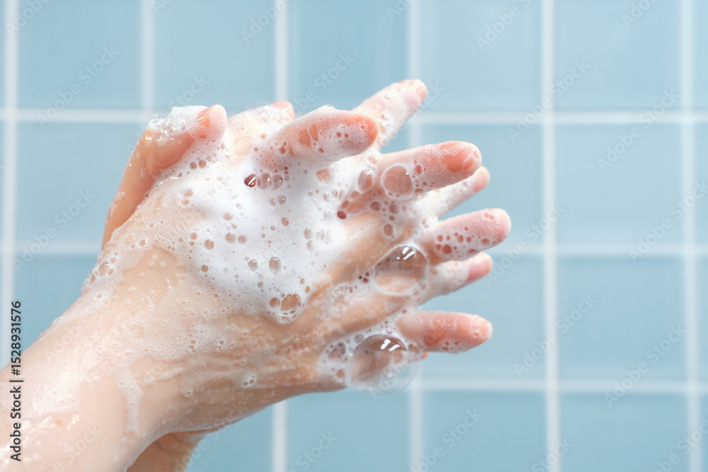 Fototapeta premium The woman washes her hands with foam against blue tiles background in bathroom side view close-up.