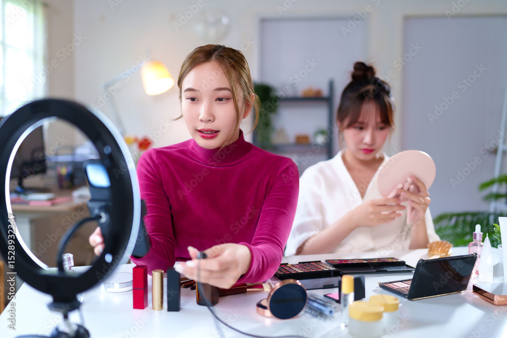Fototapeta premium Asian Women Creating Makeup Tutorial for Beauty Vlogs with Ring Light and Various Cosmetics Products for Social Media Content Creation at Home