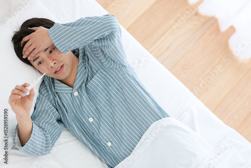 ベッドで体温を測るパジャマ姿の男性