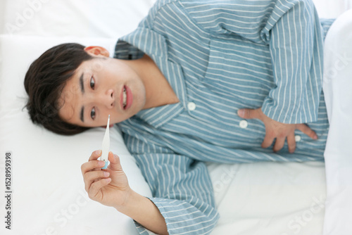 ベッドで体温を測るパジャマ姿の男性