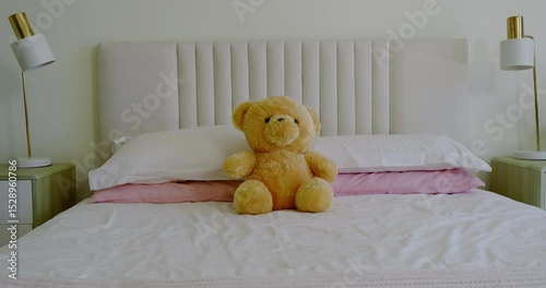 Camera is panning slowly right to frame teddy bear on bed between lamp, potted plant