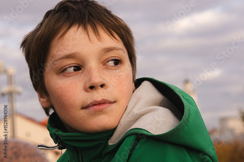 Boy in green jacket glancing sideways with soft evening light