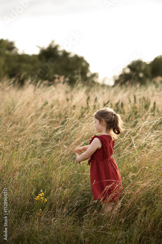 Child girl standing sideways in tall grass.