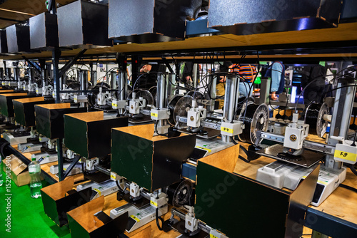 Multiple 3D printers operate simultaneously on shelves in a factory or production facility, showcasing modern manufacturing technology and automation on a large scale.