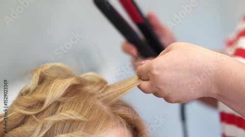 Professional hairdresser, stylist does hairstyle on short hair - uses straightener