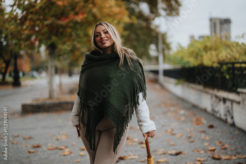 A cheerful woman dressed in cozy attire enjoying a relaxing autumn day in a park. Surrounded by colorful leaves, she holds an umbrella while walking along a pathway lined with trees.