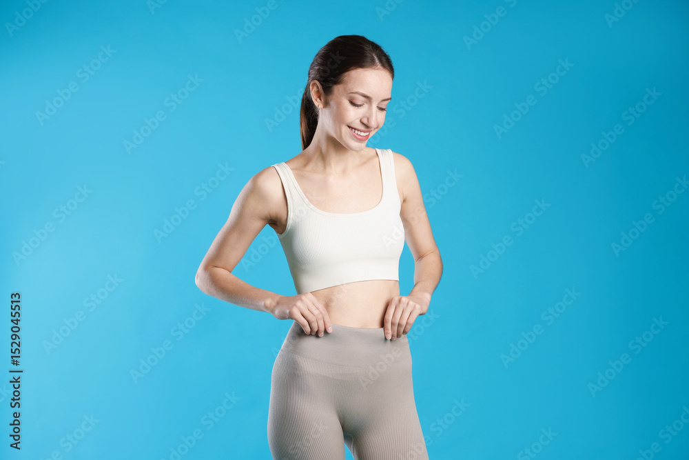 Fototapeta premium Beautiful woman with flat belly on light blue background